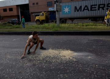 A youth moves quickly to collect grains of corn  on the street that fell from a truck that was looted outside the port in Puerto Cabello.