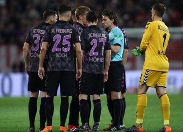 Referee Guido Winkmann is confronted by the Freiburg squad after ordering the players back onto the pitch.