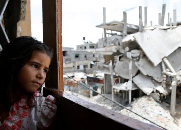 A Palestinian girl inside her family’s partially destroyed home looks at the destruction outside in the Shejaiya neighborhood of Gaza City. (File Photo)