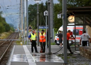 A Swiss police officer stands near workers cleaning a platform after attack on a Swiss train in Salez, Switzerland, on August 13. 