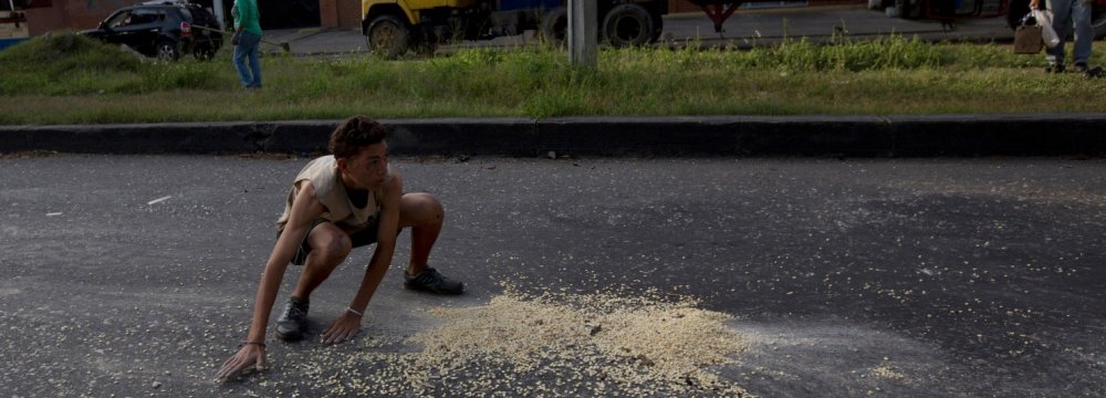 A youth moves quickly to collect grains of corn  on the street that fell from a truck that was looted outside the port in Puerto Cabello.