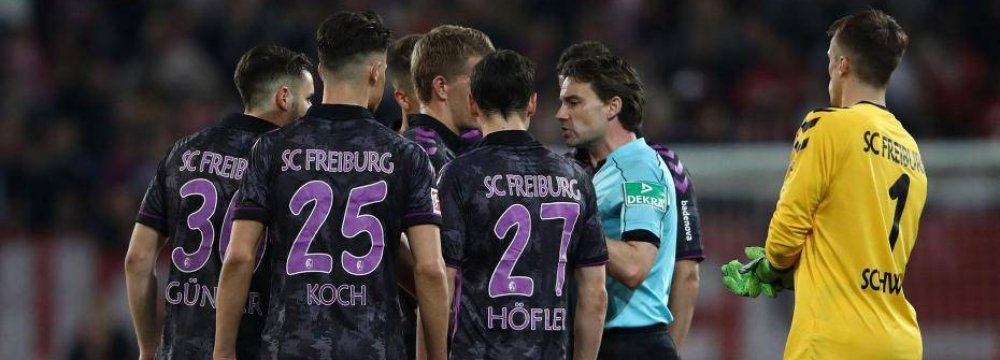 Referee Guido Winkmann is confronted by the Freiburg squad after ordering the players back onto the pitch.