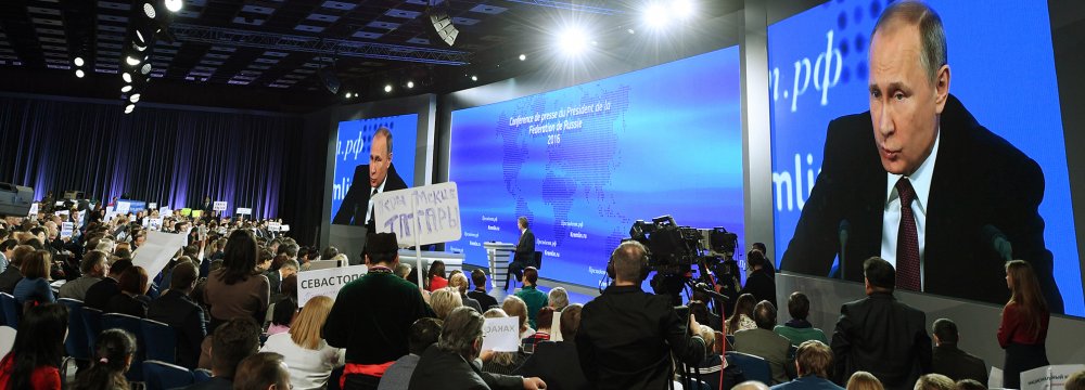 Video screens display President Vladimir Putin speaking during his annual press conference in Moscow while journalists hold the name of their media, on December 23.