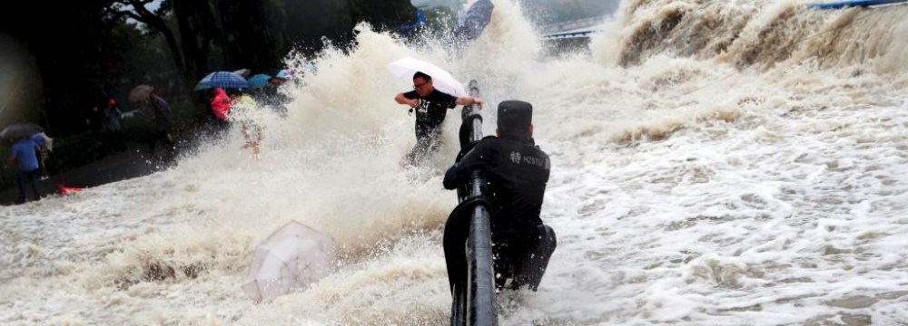 A paramilitary policeman holds onto a fence as tourists dodge tidal waves increased under the influence of Typhoon Dujuan, in Hangzhou, China, in September 2015. (File Photo)