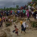 A crowd of Rohingya walk carrying aid through  a muddy refugee camp.